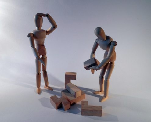 Two artist's mannequins attempting to put together a wooden cube packing puzzle.