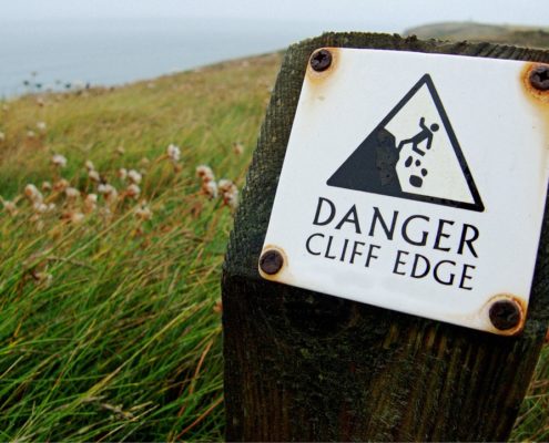 A sign at the top of a seaside cliff reads, "Danger, cliff edge."